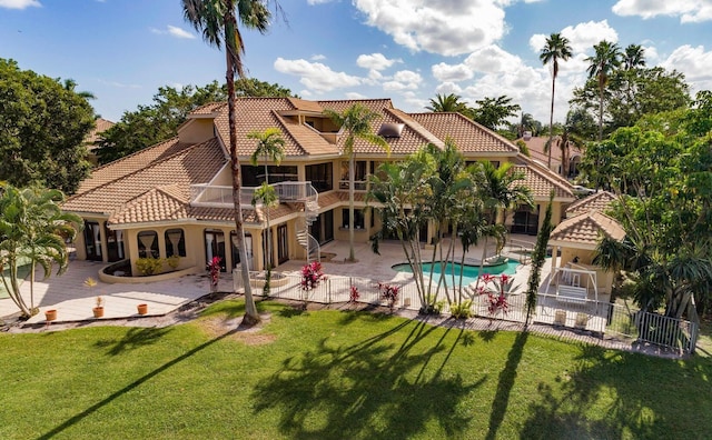 back of property with a balcony, a patio area, and a lawn