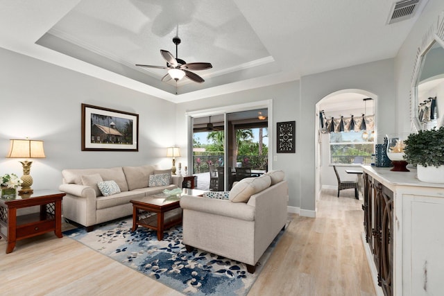 living room with ceiling fan, ornamental molding, light hardwood / wood-style flooring, and a tray ceiling