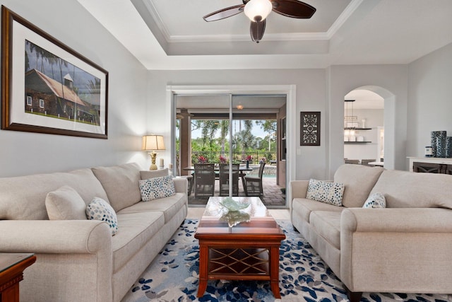 living room featuring a raised ceiling, ceiling fan, and ornamental molding