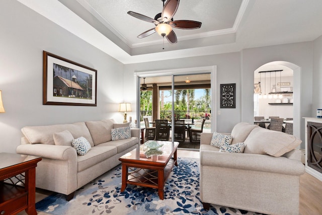 living room with ceiling fan, a raised ceiling, wood-type flooring, and ornamental molding