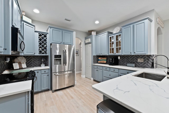 kitchen featuring decorative backsplash, light stone countertops, stainless steel appliances, sink, and light hardwood / wood-style floors