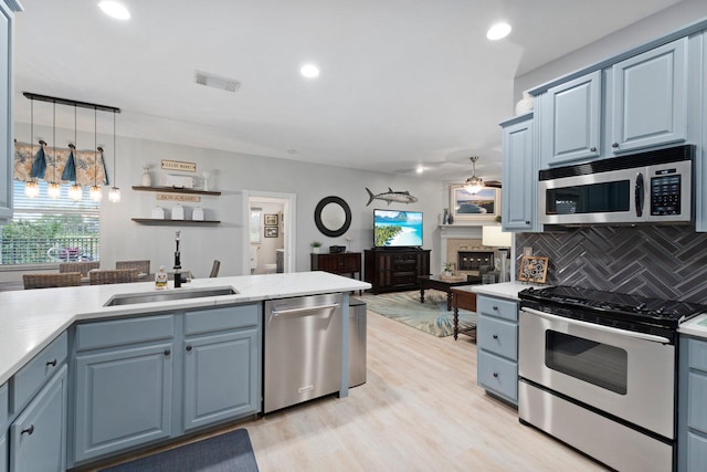 kitchen featuring backsplash, sink, blue cabinetry, decorative light fixtures, and stainless steel appliances