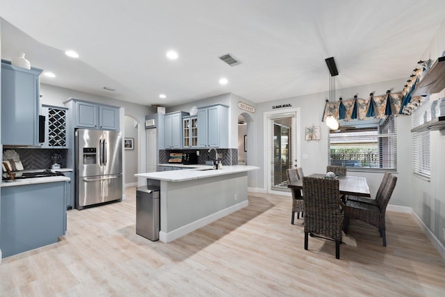 kitchen with light wood-type flooring, stainless steel refrigerator with ice dispenser, backsplash, and hanging light fixtures