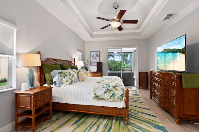 bedroom featuring access to exterior, light wood-type flooring, ornamental molding, a tray ceiling, and ceiling fan