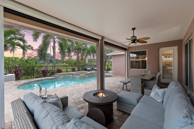 pool at dusk with an in ground hot tub, an outdoor living space with a fire pit, a patio area, and ceiling fan