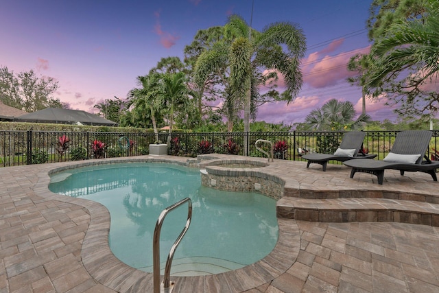 pool at dusk featuring an in ground hot tub and a patio area