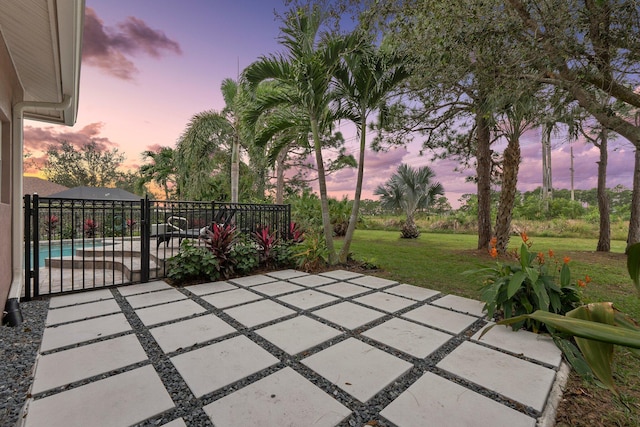 patio terrace at dusk featuring a lawn and a fenced in pool