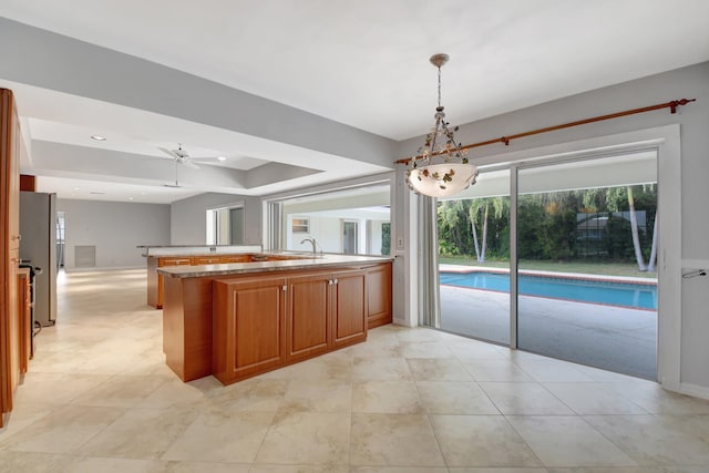 kitchen with light stone countertops, ceiling fan, kitchen peninsula, stainless steel fridge, and pendant lighting