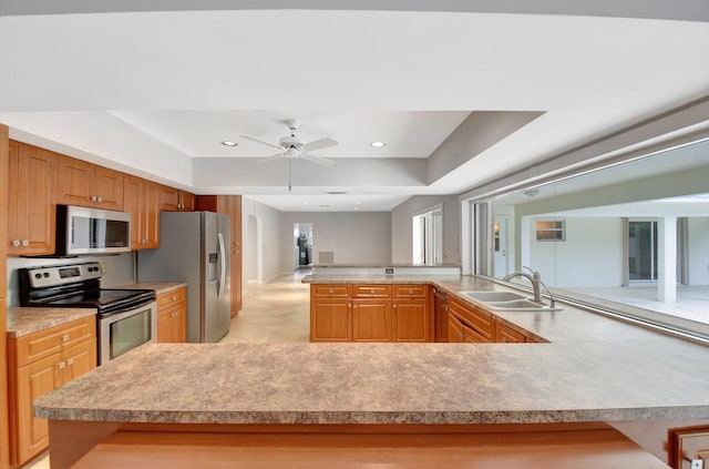 kitchen with a raised ceiling, ceiling fan, sink, and appliances with stainless steel finishes