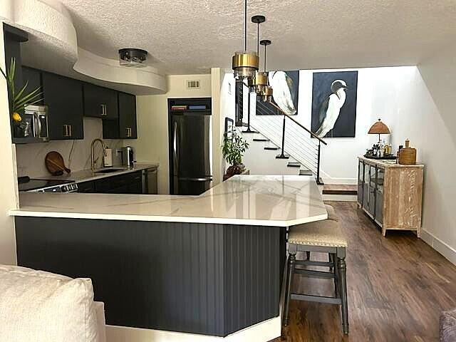 kitchen with sink, hanging light fixtures, a textured ceiling, fridge, and kitchen peninsula