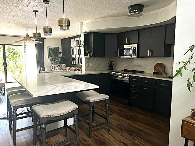 kitchen featuring kitchen peninsula, appliances with stainless steel finishes, hanging light fixtures, and a breakfast bar area