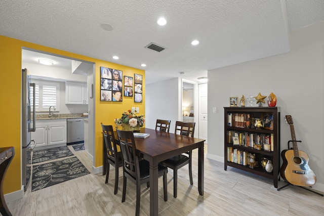 dining space with sink, a textured ceiling, and light wood-type flooring