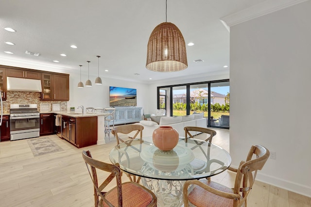 dining space with crown molding, sink, and light wood-type flooring