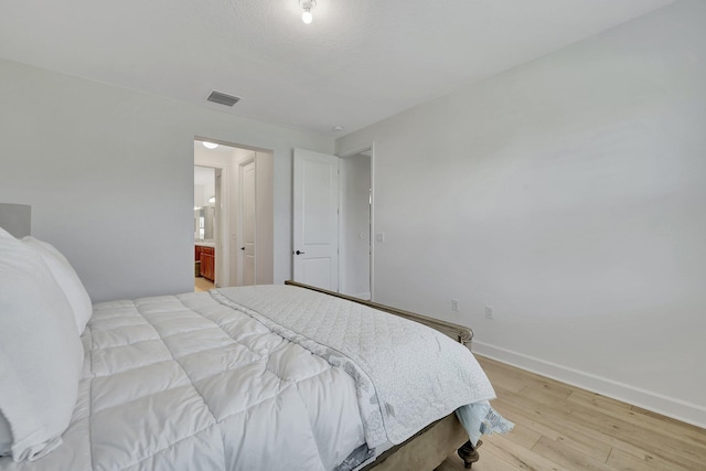 bedroom featuring connected bathroom and light hardwood / wood-style flooring