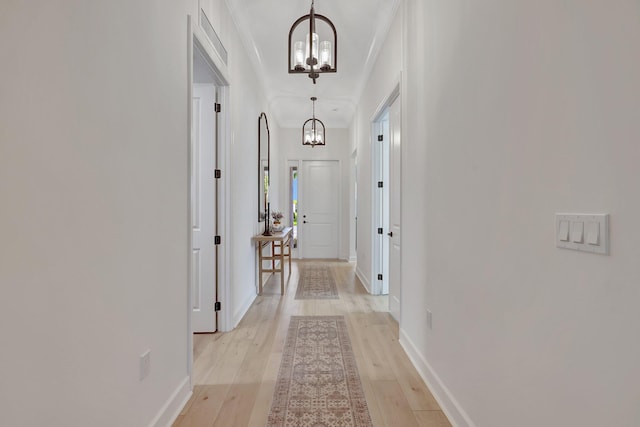 corridor with crown molding, a chandelier, and light wood-type flooring