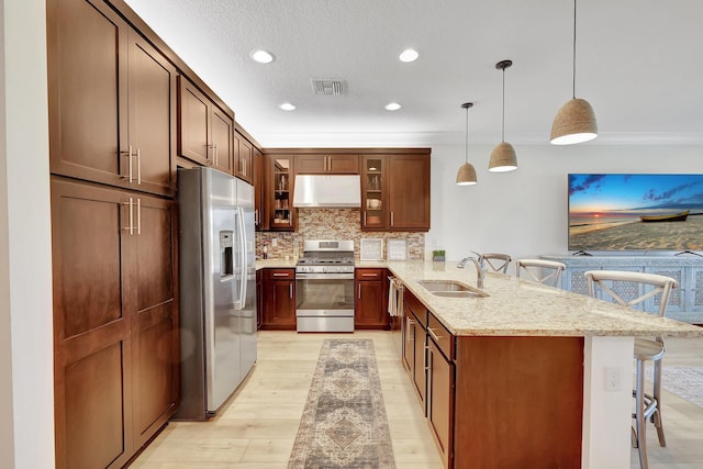 kitchen with sink, hanging light fixtures, a kitchen breakfast bar, light stone counters, and appliances with stainless steel finishes