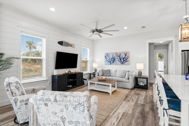 living room featuring light hardwood / wood-style flooring, ceiling fan, and wood walls