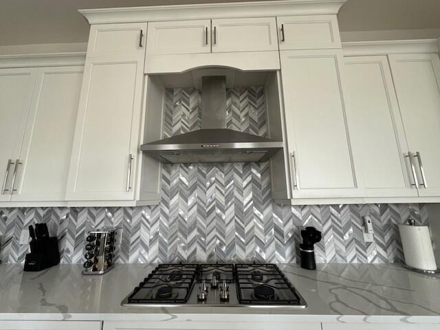 kitchen with stainless steel gas stovetop, light stone countertops, wall chimney range hood, and tasteful backsplash