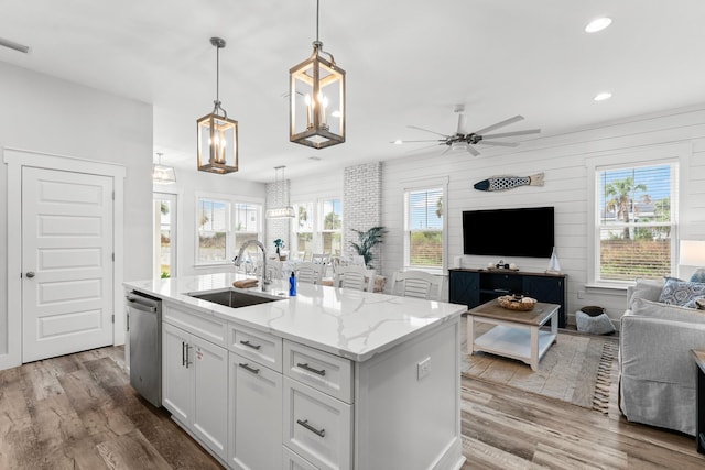 kitchen featuring pendant lighting, white cabinets, sink, stainless steel dishwasher, and an island with sink