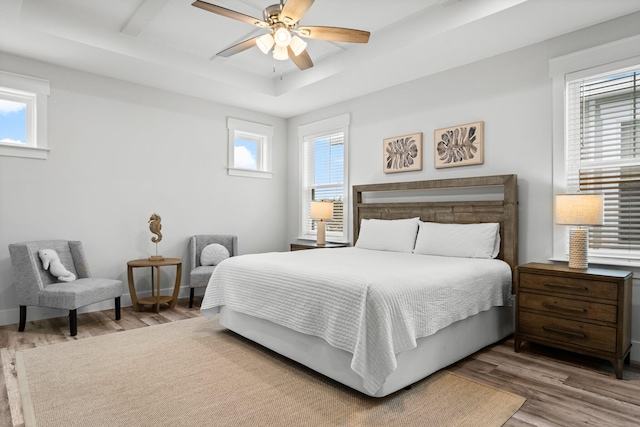 bedroom featuring hardwood / wood-style floors, ceiling fan, a tray ceiling, and multiple windows