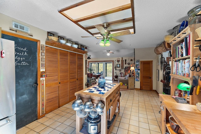 kitchen with light tile patterned floors, a textured ceiling, stainless steel refrigerator, and ceiling fan