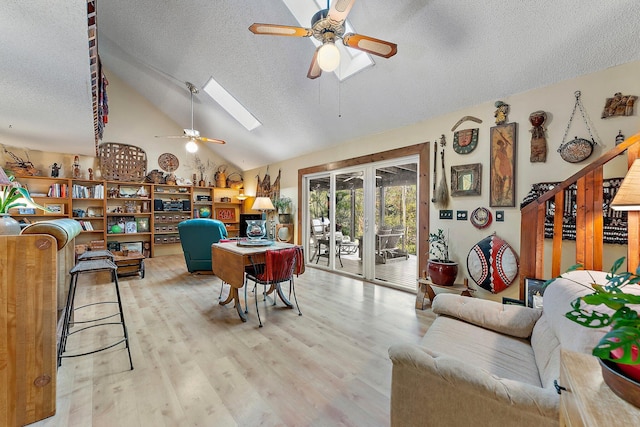 living room featuring a textured ceiling, light wood-type flooring, ceiling fan, and vaulted ceiling with skylight