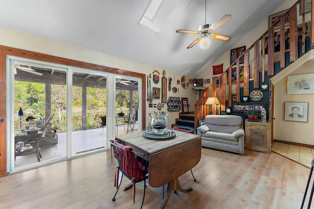 dining space featuring a textured ceiling, light hardwood / wood-style flooring, lofted ceiling with skylight, and ceiling fan