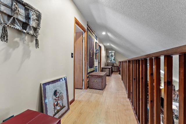 hallway with a textured ceiling, light hardwood / wood-style flooring, and vaulted ceiling