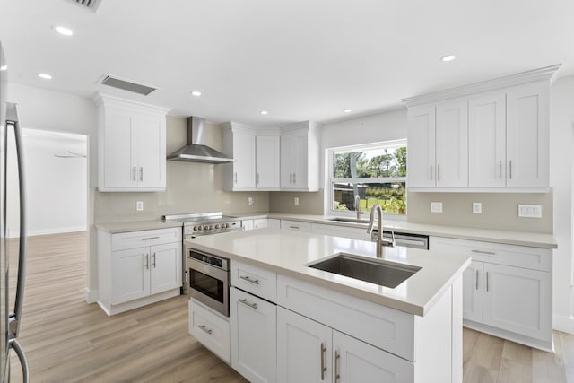 kitchen featuring white cabinets, light wood-type flooring, sink, and wall chimney range hood