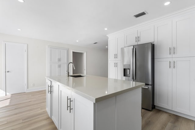 kitchen with a kitchen island with sink, white cabinets, sink, light wood-type flooring, and stainless steel fridge with ice dispenser