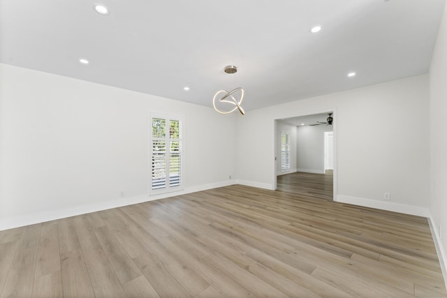 empty room with ceiling fan with notable chandelier and light hardwood / wood-style floors