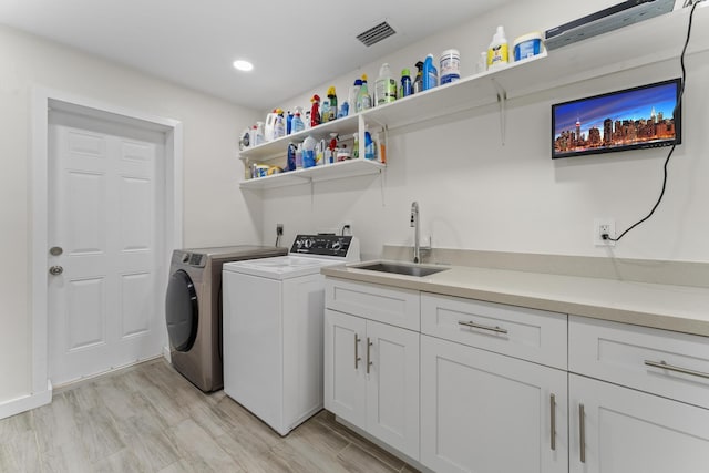 laundry area featuring cabinets, sink, light wood-type flooring, and independent washer and dryer