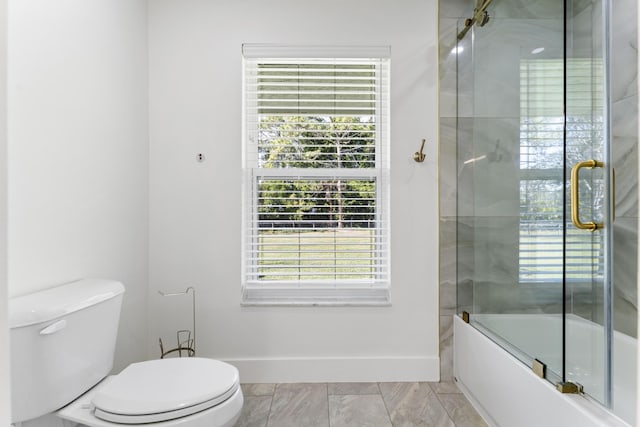 bathroom featuring toilet and bath / shower combo with glass door