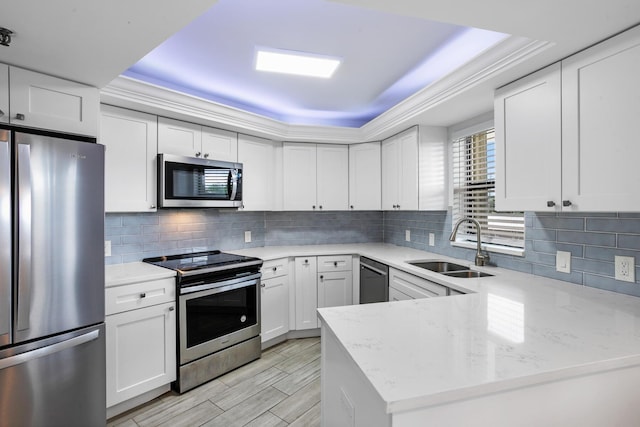 kitchen with sink, light stone countertops, appliances with stainless steel finishes, white cabinetry, and kitchen peninsula