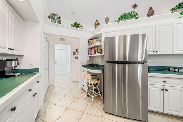 kitchen with stainless steel refrigerator, white cabinetry, and light tile patterned floors