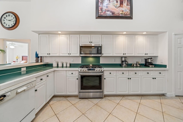 kitchen with a towering ceiling, stainless steel appliances, ceiling fan, light tile patterned floors, and white cabinetry