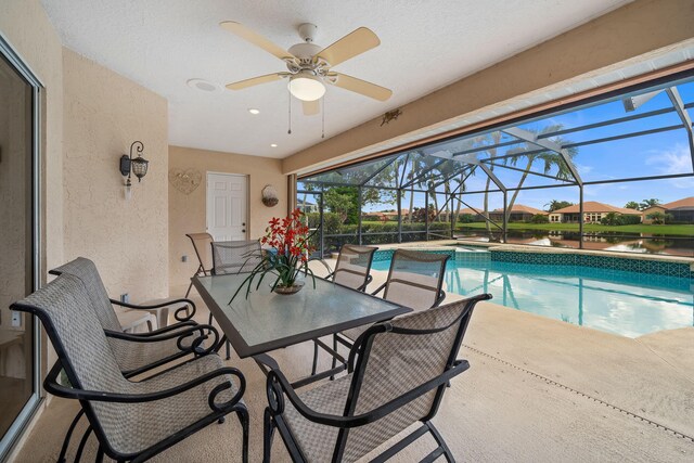 view of swimming pool with glass enclosure, ceiling fan, a patio area, and a water view