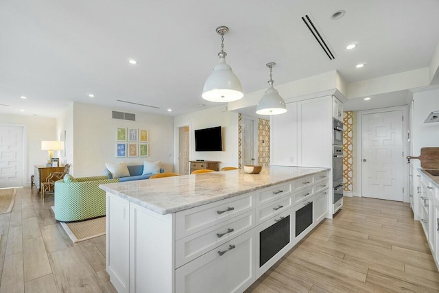 kitchen with white cabinets, pendant lighting, a kitchen island, and light stone counters