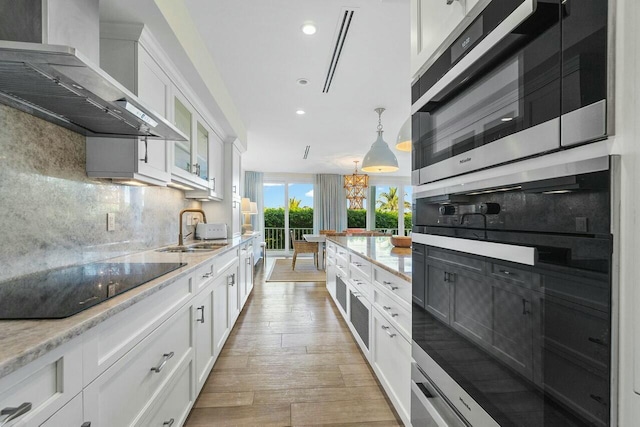 kitchen with white cabinets, stainless steel oven, sink, and wall chimney range hood