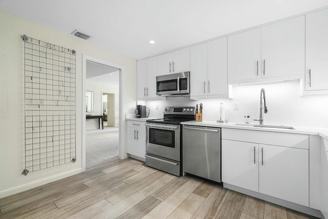 kitchen featuring sink, white cabinets, light wood-type flooring, and appliances with stainless steel finishes