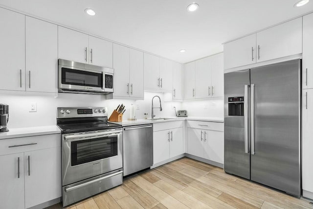 kitchen with appliances with stainless steel finishes, light hardwood / wood-style floors, white cabinetry, and sink