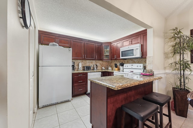 kitchen with a kitchen breakfast bar, kitchen peninsula, light tile patterned floors, and white appliances