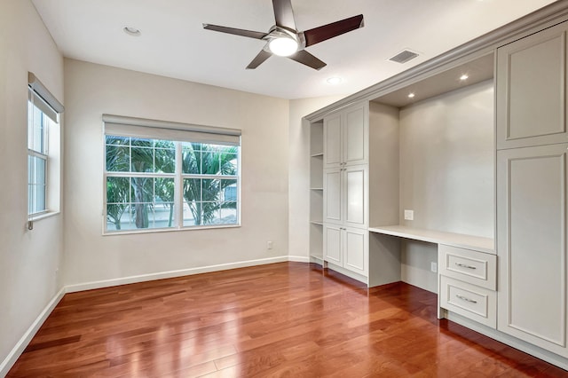 unfurnished bedroom featuring a closet, built in desk, hardwood / wood-style flooring, and ceiling fan