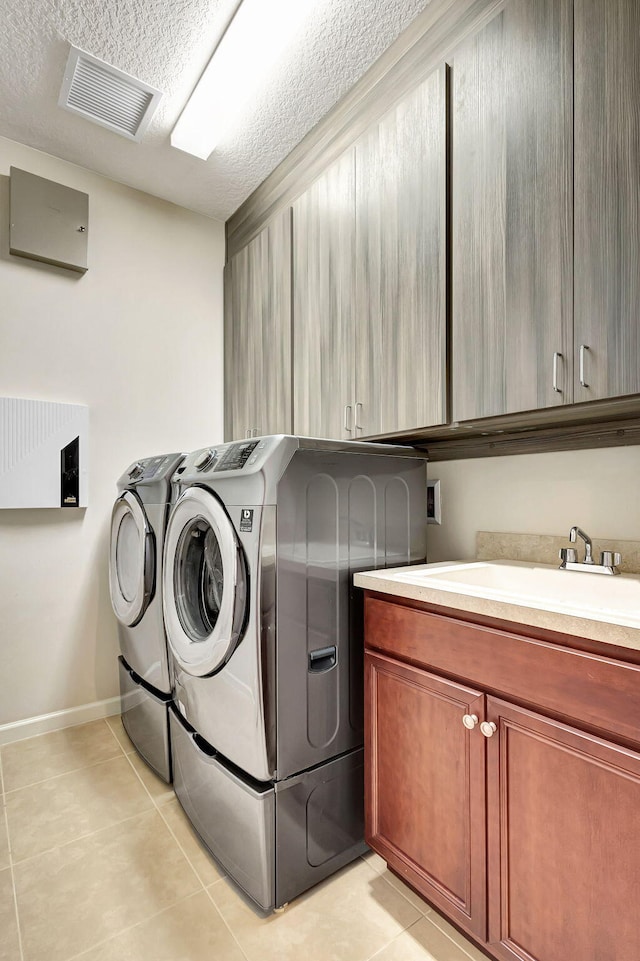 laundry room with cabinets, a textured ceiling, sink, washing machine and dryer, and light tile patterned flooring