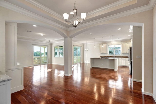 unfurnished living room with a healthy amount of sunlight, an inviting chandelier, and crown molding