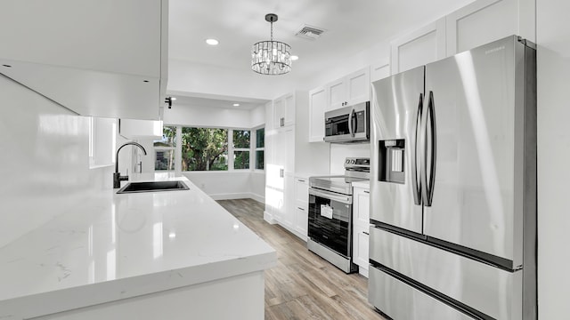 kitchen with light stone counters, stainless steel appliances, sink, a notable chandelier, and white cabinetry