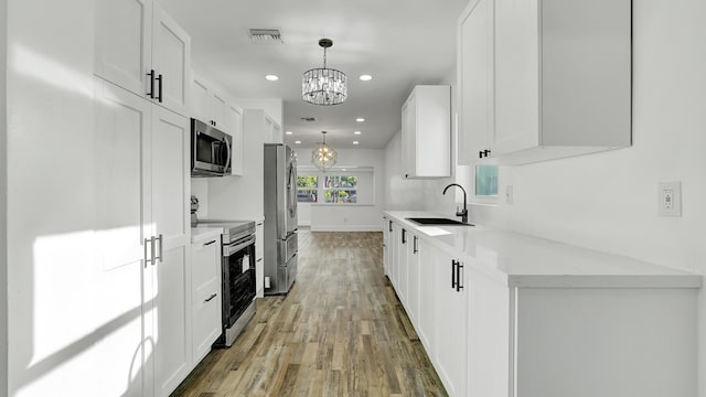 kitchen featuring sink, appliances with stainless steel finishes, decorative light fixtures, white cabinetry, and a chandelier