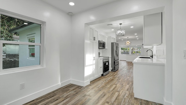 kitchen with appliances with stainless steel finishes, light wood-type flooring, sink, pendant lighting, and white cabinetry