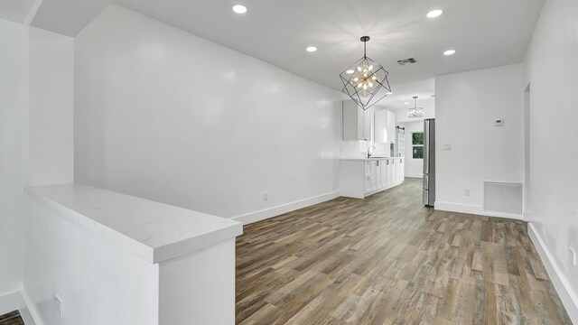 unfurnished living room with wood-type flooring, a notable chandelier, and sink