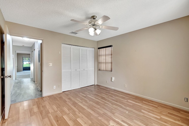 unfurnished bedroom featuring a closet, ceiling fan, light hardwood / wood-style flooring, and a textured ceiling